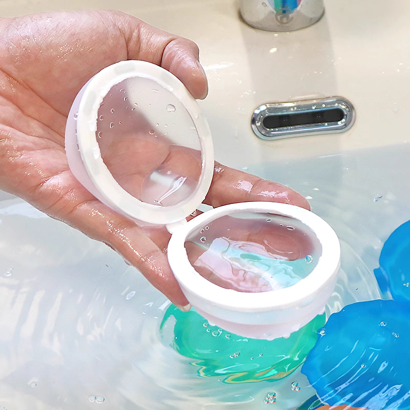 Hand holding a white magnetic water balloon open over a sink filled with water.
