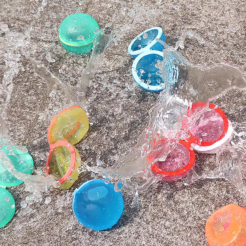 Colorful plastic water balloons splashing in water on a gravel surface