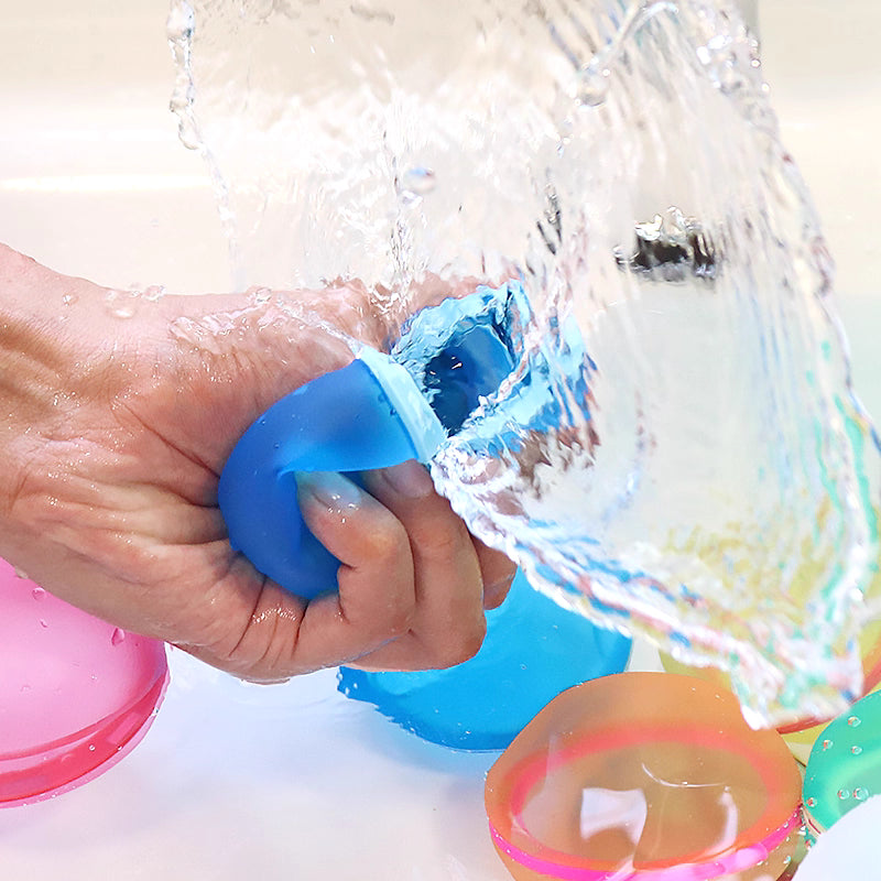 Hand squeezing a blue water balloon into water with colorful water balloons around.